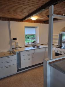 cocina con armarios blancos, fregadero y ventana en A cozy house to stay en Vandel