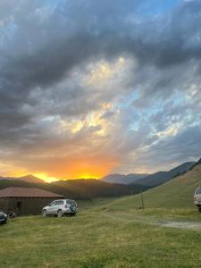 un coche aparcado en un campo con la puesta de sol en el fondo en Above the Clouds en Tusheti