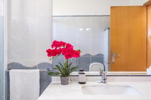 a bathroom with a sink with a vase with red flowers at Casa Flor do Campo in Calheta +20 photos