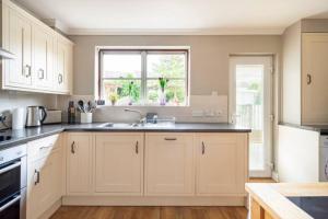 cocina con armarios blancos, fregadero y ventana en River view cottage, in Cockermouth center en Cockermouth