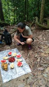 Ein Mann, der neben einem Tisch mit Essen kniet. in der Unterkunft Bukit Lawang Glamping & Jungle Trekking in Bukit Lawang