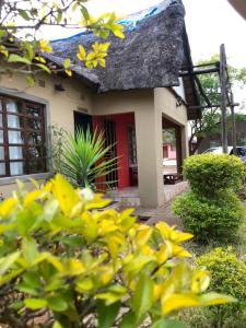 ein kleines Haus mit einer roten Tür und gelben Blumen in der Unterkunft Ntshe River Lodge in Francistown
