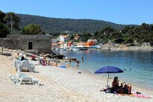 a group of people sitting on a beach with an umbrella at Apartments by the sea Veli Losinj, Losinj - 15229 in Veli Lošinj