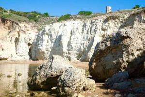 uma grande rocha sentada na praia junto à água em Superior Apartment le Case del Sole Licata em Licata