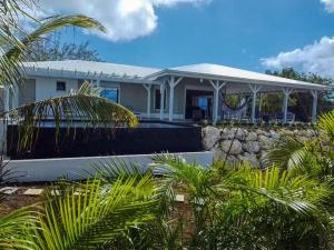 a white house with a stone wall and palm trees at Magnifique Villa Standing vue mer et proche plage in Saint-François