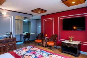 a bedroom with a red wall with a tv and chairs at Mount Conifer Suites & Spa in Darjeeling