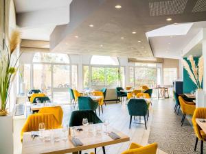 a restaurant with tables and yellow chairs and windows at Mercure Vienne Sud Chanas in Chanas