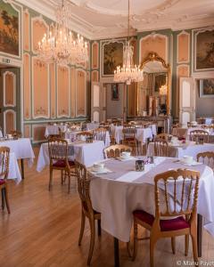 un comedor con mesas y sillas blancas y lámparas de araña en Grand Hotel De La Reine - Place Stanislas, en Nancy