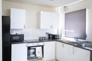 a kitchen with white cabinets and a black microwave at RUTLAND HOUSE 10 mins from Manchester City Ctr 4-Bedroom House in Manchester