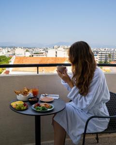 a woman sitting at a table with a plate of food at The 1932 Hotel & Spa Cap d'Antibes - MGallery Collection in Juan-les-Pins