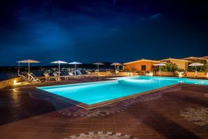 una piscina por la noche con sillas y sombrillas en Appartamenti Marineledda Golfo di Marinella en Golfo Aranci