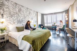 una mujer sentada en una cama en una habitación de hotel en Apartosuites Jardines de Sabatini, en Madrid