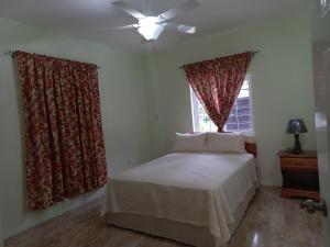 a bedroom with a bed and a window with curtains at Stoney Gate Cottages in Negril