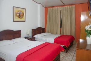 two beds in a hotel room with red and white sheets at Hotel San José in Piura