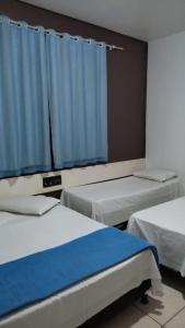 a room with three beds and a blue curtain at Hotel Foz Brasil in Foz do Iguaçu