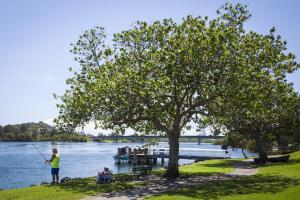 a woman standing under a tree fishing on the river at Colonial Tweed Holiday & Home Park in Tweed Heads