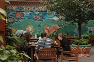 un grupo de personas sentadas en una mesa frente a un mural en Tibet Guest House, en Katmandú