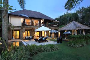 a house with a porch and a patio with chairs and an umbrella at Villa Arjuna in Tanah Lot