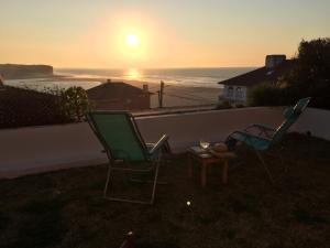 two chairs and a table with the sunset in the background at Foz - Sea View Cottage in Foz do Arelho