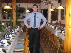 a man in a shirt and tie standing in front of tables at Syrtaki bei Nikos in Schopfloch