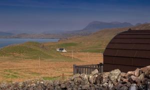 a barn in the middle of a field next to the water at Culkein Pods in Lochinver