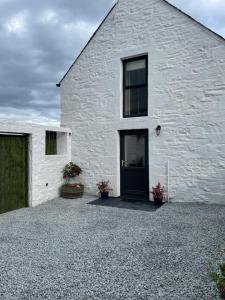 a white house with a black door on a gravel driveway at Cozy 2 bedroom cottage with log burner close to Loch Ken in New Galloway