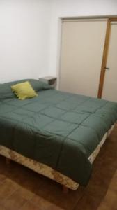a bed with a green comforter and a yellow pillow at Departamento Los Inmigrantes in Esquel