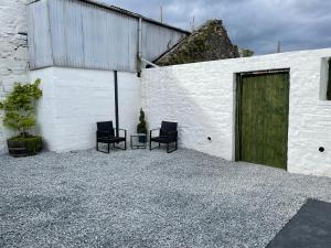 a white building with two chairs and a green door at Cozy 2 bedroom cottage with log burner close to Loch Ken in New Galloway