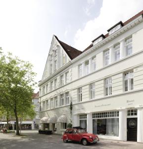 une vieille voiture rouge garée devant un bâtiment blanc dans l'établissement Hotel & Café KleinerGrünauer, à Bad Salzuflen