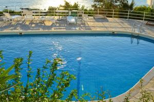 a large blue swimming pool with chairs and the water at Anavissos Panoramic sea view apt with shared pool in Anavyssos
