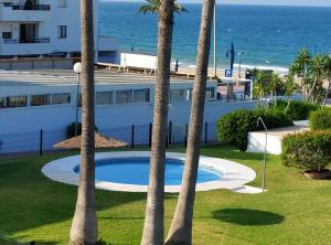basen z palmami przed budynkiem w obiekcie Precioso apartamento en primera línea de playa de la Barrosa w mieście Chiclana de la Frontera