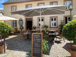un patio con mesas, sillas y una sombrilla en Warsberger Weinhof - Hotel & Weinwirtschaft, en Neumagen-Dhron