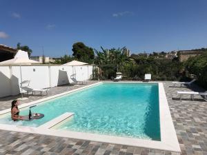 a woman is sitting next to a swimming pool at Villa Santa Venera in Marsala