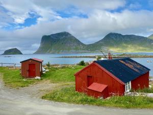 two red buildings in a field next to a body of water at Haukland Camp Cabin in Leknes