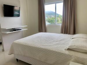 1 dormitorio con 1 cama, TV y ventana en Res Costa Verde, en Bombinhas