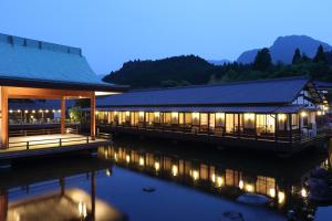 a building with lights on the water at night at Tawarayama Onsen Ryokan Minawa in Minami Aso