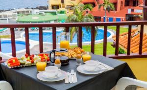 a table with breakfast food on a balcony with a pool at Apartamentos TAMARAGUA in Breña Baja