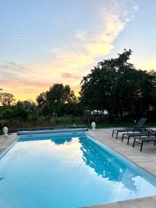 ein blauer Pool mit zwei Bänken und Sonnenuntergang in der Unterkunft La Grange 1743 