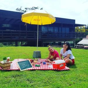 Due ragazze sedute su una coperta da picnic sotto un ombrello di Pousada Farol do Arvoredo a Governador Celso Ramos