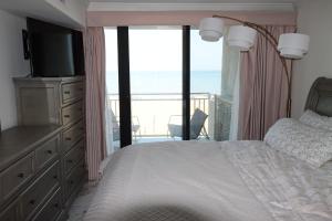 a bedroom with a bed with a television and a balcony at Oceanfront beach, sky, & dolphins in Virginia Beach