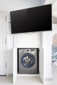 TV por encima de una lavadora en una lavandería blanca en La Fula Beach Rooms, en El Pris