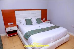 a bedroom with a large white bed with a wooden headboard at Luxe Furnished Apartments in Meru