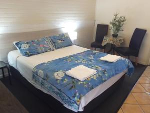 a bedroom with a bed with a blue blanket and two chairs at Paradise Motel in Mackay