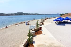 ein Strand mit blauen Sonnenschirmen und Menschen am Strand in der Unterkunft Rooms with a parking space Sibenik - 13739 in Šibenik