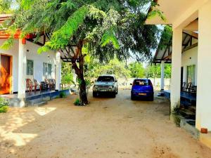 two cars parked next to a building with a tree at Hotel krish in Kalkudah