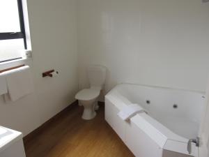 a white bathroom with a toilet and a bath tub at Abode Motel in Palmerston North