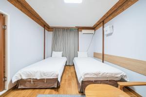 two beds in a room with wooden floors and white walls at Jeju Miju Hotel in Jeju