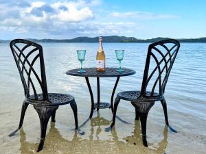 two chairs and a table with a bottle and wine glasses on the beach at Le Grand Bleu in Amami