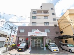a building with cars parked in front of it at Tabist Rays Hotel Yakata in Miyazaki