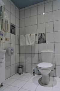 a white tiled bathroom with a toilet and towels at Alex Hotel on Dybenko in Saint Petersburg